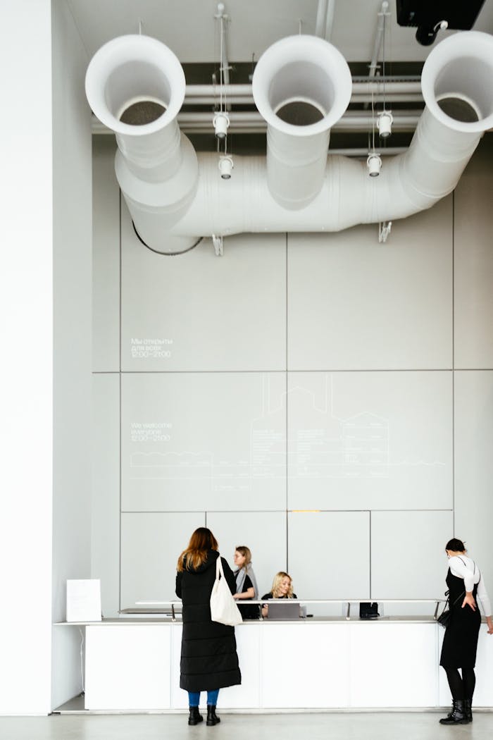 A contemporary office reception area with visible ceiling pipes and people standing.